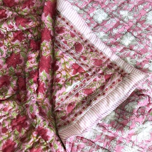 Peut inclure: Couverture rose à motifs floraux avec un motif répété de grandes fleurs rouges et de feuilles vertes. La couverture a une bordure rayée et un motif floral au verso. La couverture est en tissu matelassé doux.