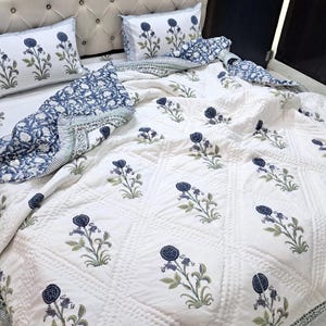 May include: White cotton quilt with a blue floral pattern. The quilt is quilted in a diamond pattern and has a white border.