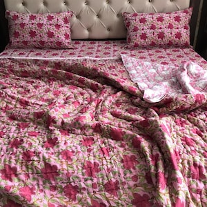 Könnte beinhalten: Eine rosafarbene Steppdecke mit floralem Muster, ein weißes Laken mit floralem Muster und zwei rosafarbene Kissenbezüge mit floralem Muster. Die Steppdecke ist aus Baumwolle und perfekt für ein Schlafzimmer.