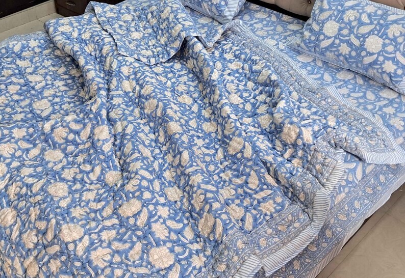 May include: A blue and white floral patterned quilt set. The bedding features a repeating pattern of flowers and leaves in white against a light blue background. The set includes a quilt and pillowcases.