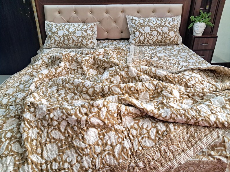 May include: A bed set featuring a floral pattern in white and tan. The set includes a comforter and two pillowcases. The bed is made up with the comforter and pillowcases, ready for use.