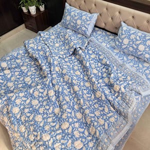 May include: A blue and white floral patterned bedding set, including a comforter, fitted sheet, and two pillowcases. The floral design features white flowers and leaves on a light blue background. The bed is made up with the bedding set.