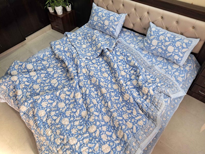 May include: A blue and white floral patterned bedding set, including a comforter, fitted sheet, and two pillowcases. The floral design features white flowers and leaves on a light blue background. The bed is made up with the bedding set.