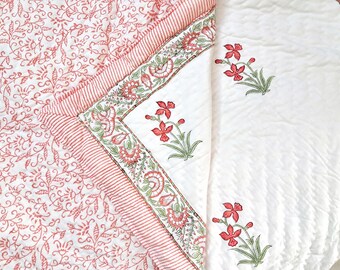 May include: A quilted textile featuring a white base with a dense red floral vine pattern on one side and a white surface with scattered red floral sprigs on the other. A decorative border with red stripes and floral motifs separates the two sides.
