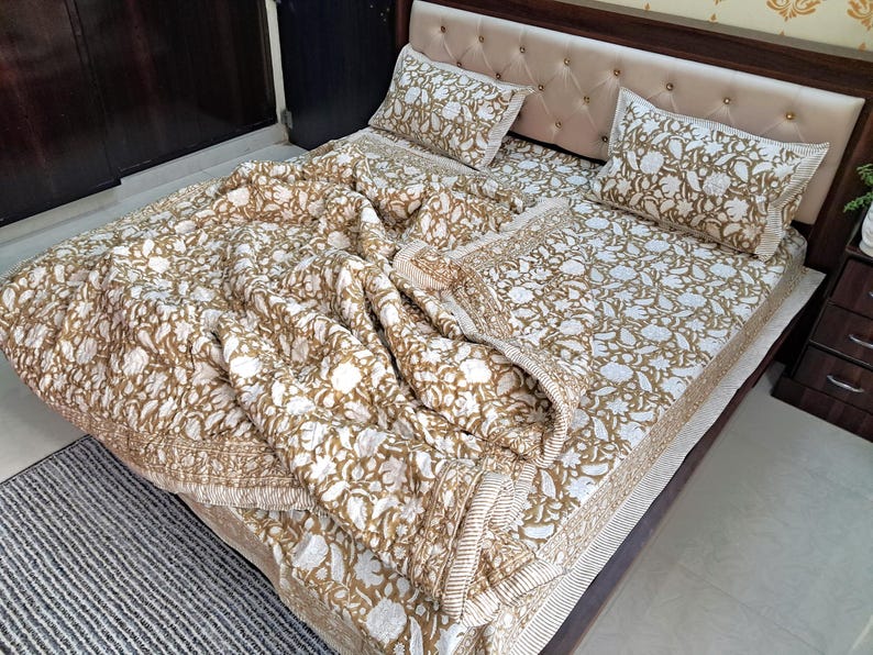 May include: A bed is made with a floral patterned quilt, matching pillowcases, and a fitted sheet. The bedding features a white background with a repeating pattern of brown flowers and leaves. The bed frame is dark brown.