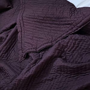 Könnte beinhalten: Eine dunkelviolette Steppdecke mit strukturierter Oberfläche. Die Decke ist gefaltet und über ein Bett gelegt.
