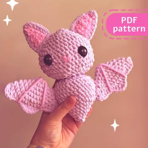 May include: A crocheted purple bat with pink ears and wings. The bat has black eyes and a pink nose. The text "PDF pattern" is in the upper right corner of the image.