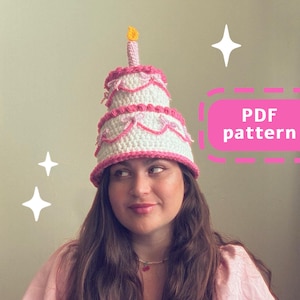 Peut inclure: Un chapeau en crochet en forme de gâteau rose et blanc avec une bougie jaune sur le dessus. Le chapeau est porté par une personne aux longs cheveux bruns. Le texte "PDF pattern" est dans une boîte rose avec une bordure en pointillés.