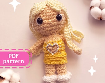 Peut inclure: Patron de poupée au crochet en PDF. La poupée porte une robe jaune avec un cœur scintillant et a les cheveux blonds. La poupée est debout sur un fond blanc avec des fleurs de coton.