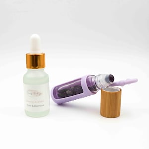Könnte beinhalten: Eine klare Glasflasche mit weißer Pipette und goldener Kappe, neben einer lila Rollerflasche mit Bambusdeckel. Die Rollerflasche enthält kleine, dunkle Steine. Auf dem Etikett steht "Funky Healing" und "Care & Remove".