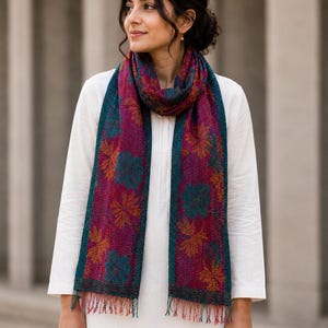 May include: A colorful scarf with a floral pattern. The scarf features a deep magenta center with teal and orange floral designs, framed by teal borders. The scarf has a fringed edge.