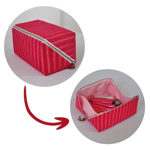 Peut inclure: Une trousse de maquillage zipp&eacute;e &agrave; rayures roses avec une doublure rose. La trousse est ouverte et remplie de pinceaux de maquillage.