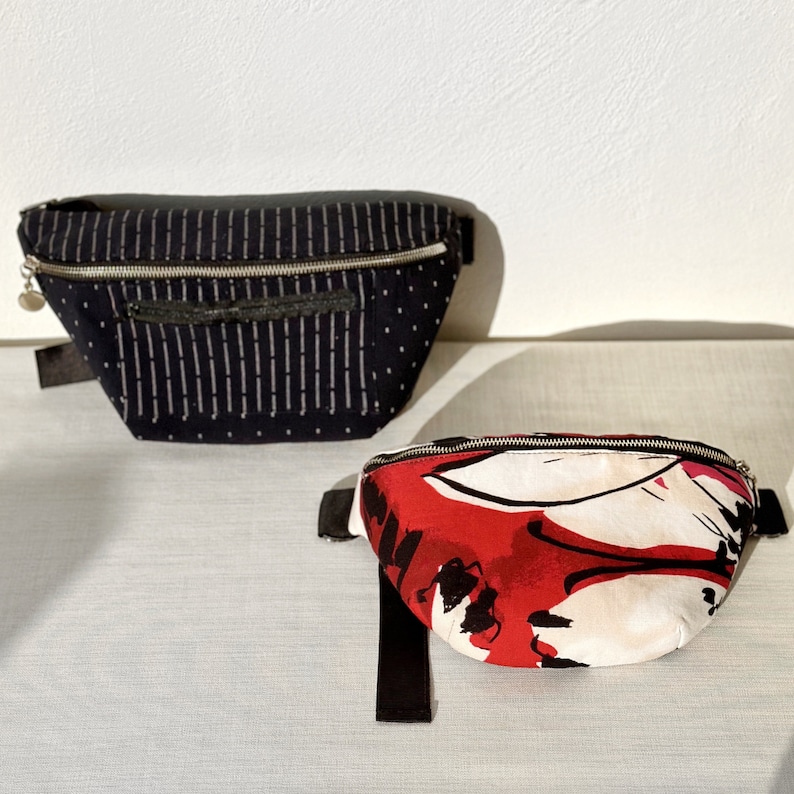 K&ouml;nnte beinhalten: Zwei Bauchtaschen, eine schwarze mit wei&szlig;en Streifen und eine rote mit einem abstrakten Muster in Wei&szlig; und Schwarz.