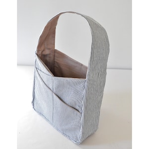 May include: A blue and white striped tote bag with a single strap. The bag has multiple pockets on the front.