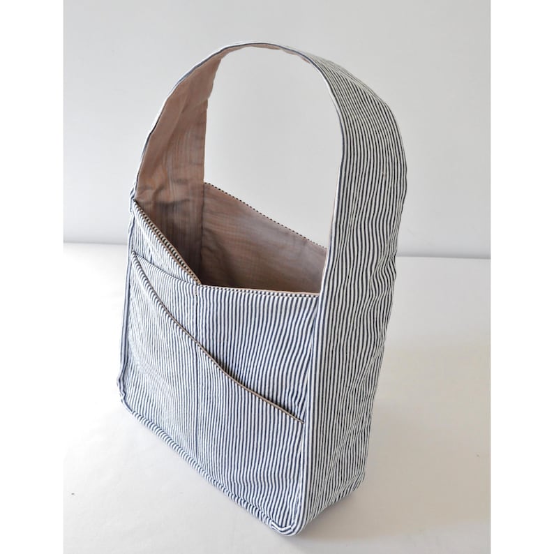 May include: A blue and white striped tote bag with a single strap. The bag has multiple pockets on the front.
