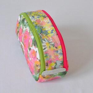 May include: A floral print cosmetic bag with a zipper closure. The bag has a green and pink trim and a white leather patch on the bottom.