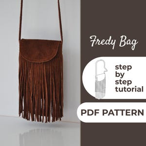 Puede incluir: Un bolso bandolera de ante marrón con flecos, cierre de solapa y correa larga. El bolso cuelga contra una pared blanca. El texto "Fredy Bag" y "PDF PATTERN" son visibles.