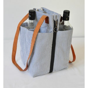 Puede incluir: Una bolsa de lona rayada azul y blanca con asas de cuero marr&oacute;n y cierre de cremallera. La bolsa tiene dos bolsillos separados en la parte delantera y est&aacute; dise&ntilde;ada para llevar dos botellas.
