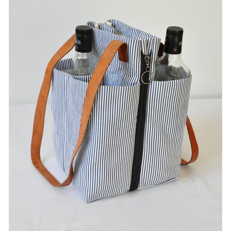 Puede incluir: Una bolsa de lona rayada azul y blanca con asas de cuero marr&oacute;n y cierre de cremallera. La bolsa tiene dos bolsillos separados en la parte delantera y est&aacute; dise&ntilde;ada para llevar dos botellas.