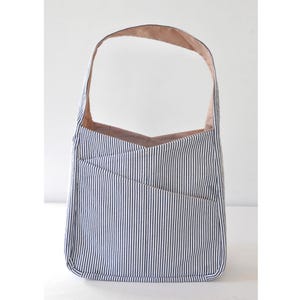 May include: A blue and white striped tote bag with a pink lining and a single strap. The bag has a unique design with a V-shaped opening and a pocket on the front.