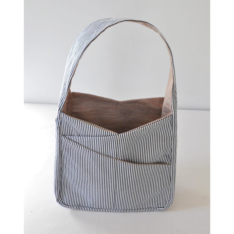 May include: A small, blue and white striped tote bag with a zipper closure and a single handle. The bag has a light brown lining and a pocket on the front.