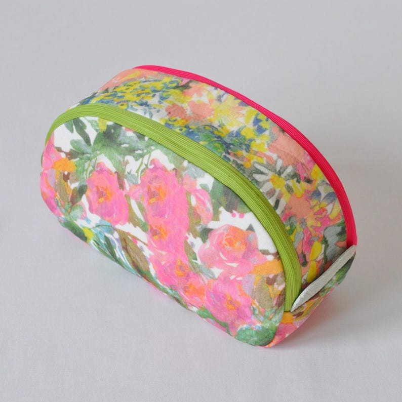 May include: A floral print cosmetic bag with a green and pink trim. The bag is oval shaped and has a zipper closure.