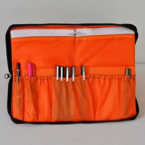 May include: Orange zippered pouch with multiple compartments for holding pens and pencils. The pouch is made of a durable fabric and has a black zipper.
