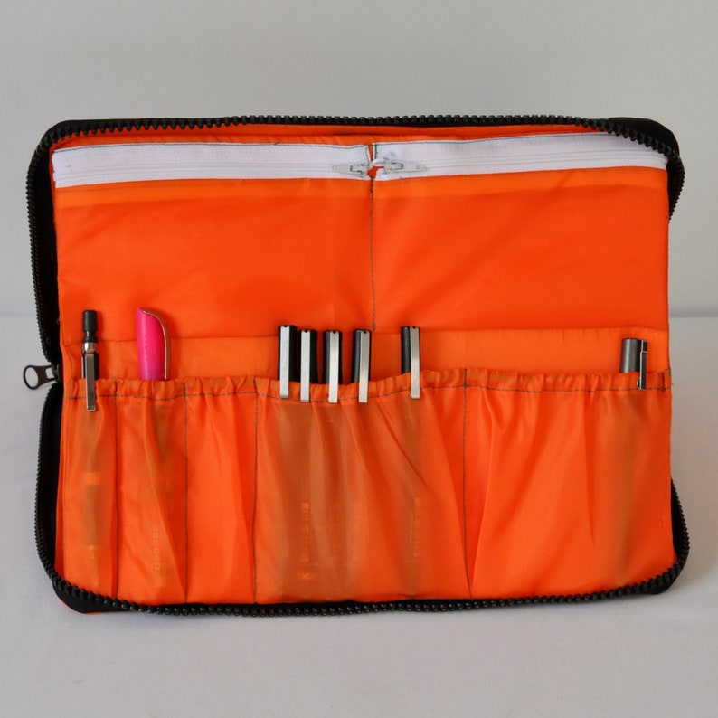 May include: Orange zippered pouch with multiple compartments for holding pens and pencils. The pouch is made of a durable fabric and has a black zipper.