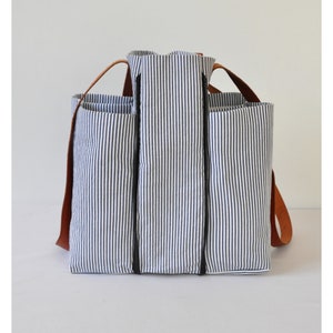 Puede incluir: Una bolsa de lona rayada azul y blanca con correas de cuero marr&oacute;n y cierres de cremallera negros.
