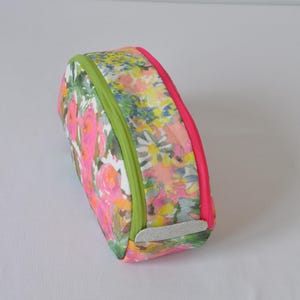 May include: A floral print makeup bag with a green and pink zipper. The bag is oval shaped and has a white fabric lining.
