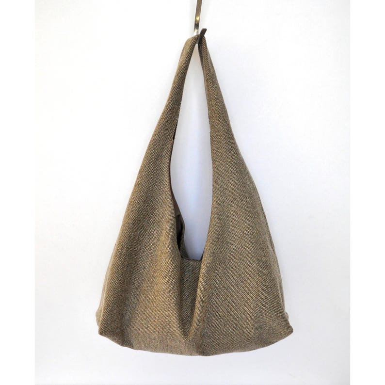 Pu&ograve; includere: Una borsa tote in tweed marrone con un solo cinturino. La borsa &egrave; appesa a un gancio su una parete bianca.