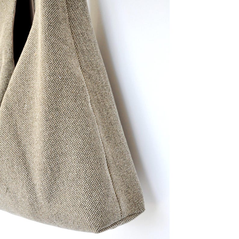 Pu&ograve; includere: Una borsa tote in tela beige di forma triangolare. La borsa &egrave; realizzata in tessuto strutturato e ha un design semplice.