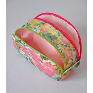 May include: A floral print makeup bag with two separate compartments, each with a pink zipper and a green lining. The bag is open to reveal the pink lining.