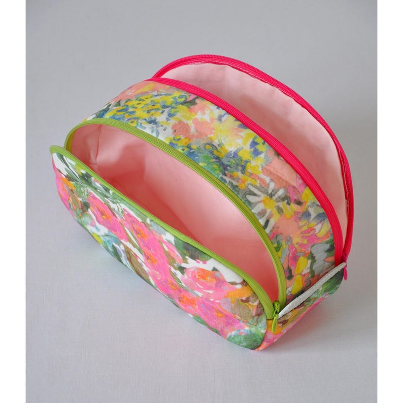 May include: A floral print makeup bag with two separate compartments, each with a pink zipper and a green lining. The bag is open to reveal the pink lining.