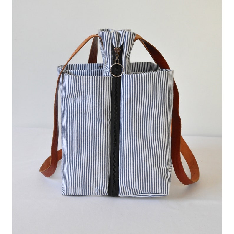 Puede incluir: Una bolsa de mano a rayas con asas de cuero marr&oacute;n y cierre de cremallera. La bolsa tiene un patr&oacute;n de rayas azules y blancas.