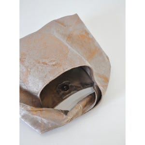 May include: A beige tote bag with a soft, velvety texture and a subtle, marbled pattern in shades of gold. The bag features a single handle and a magnetic snap closure. The interior is a darker brown colour.