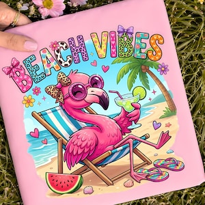 Summer Flamingo Beach Vibes tshirt png. Pink, purple, green, blue, yellow and orange bold pretty beach vibes writing, the words say BEACH VIBES, each letter is a different color with a pattern, leopard print, cow print, hearts, and flowers, and there are coquette bows on some of the letters. Underneath the words is a preppy pink flamingo, sitting in a beach chair at the beach, she is holding a margarita cocktail drink, and she has watermelon and flip flops nearby. sunny summer beach vibe fun