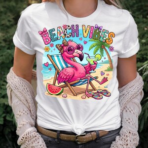 May include: White t-shirt featuring a cartoon flamingo wearing sunglasses, relaxing on a beach chair, and holding a cocktail. The shirt has the words "Beach Vibes" in colorful letters, along with beach-themed graphics like a watermelon slice and palm tree.