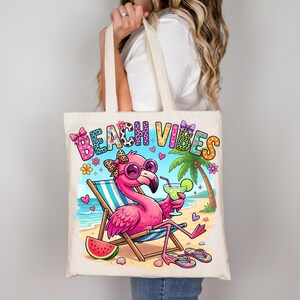 May include: A cream-colored tote bag featuring a pink flamingo wearing sunglasses and holding a cocktail, relaxing on a beach chair. The words "Beach Vibes" are printed across the top. A watermelon slice and flip-flops are also visible.