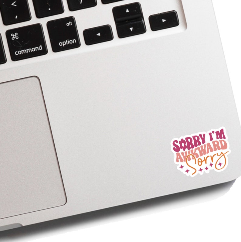 May include: A pink and white sticker with the text "Sorry I'm Awkward Sorry" on a silver laptop.