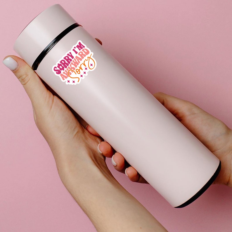 May include: A pink stainless steel water bottle with a sticker that says "Sorry I'm Awkward Sorry" in pink and orange letters with a pink heart and stars.