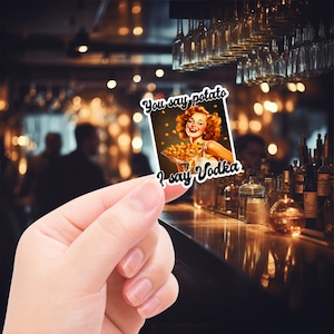 May include: A sticker with a retro-style illustration of a woman holding a martini glass filled with potato chips. The text on the sticker reads "You say potato I say Vodka".