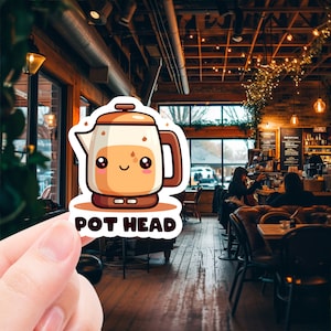 May include: A cartoon sticker of a brown and white coffee pot with a smiling face. The sticker says "Pot Head" in black text.