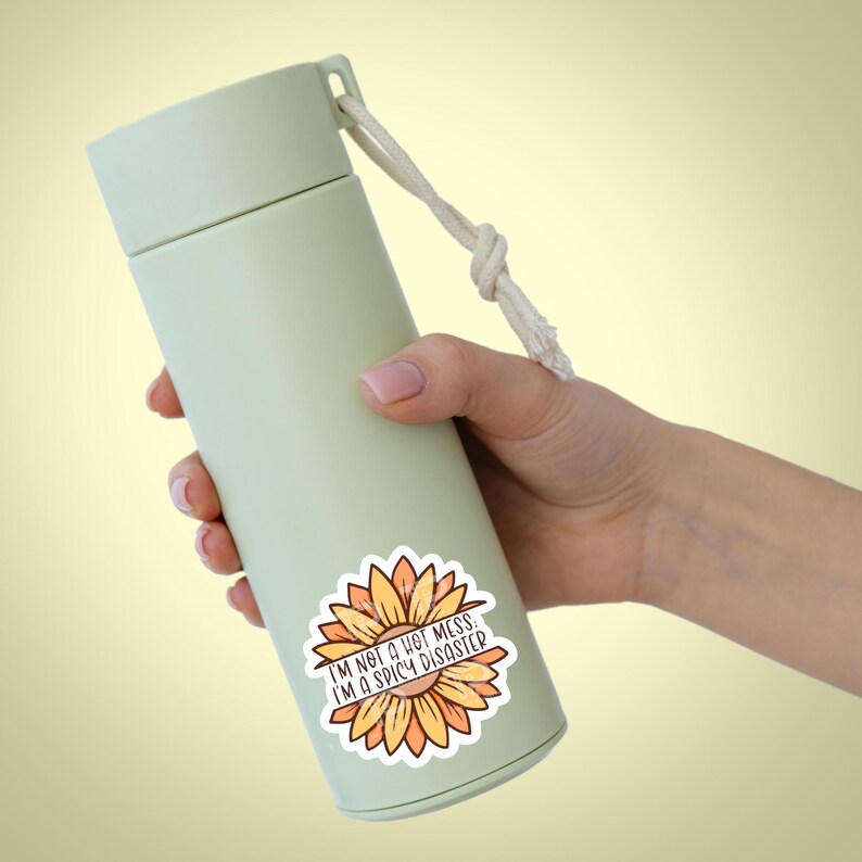 May include: A green reusable water bottle with a white rope handle and a sticker that says "I'm not a hot mess. I'm a spicy disaster." The sticker features a yellow and orange sunflower.