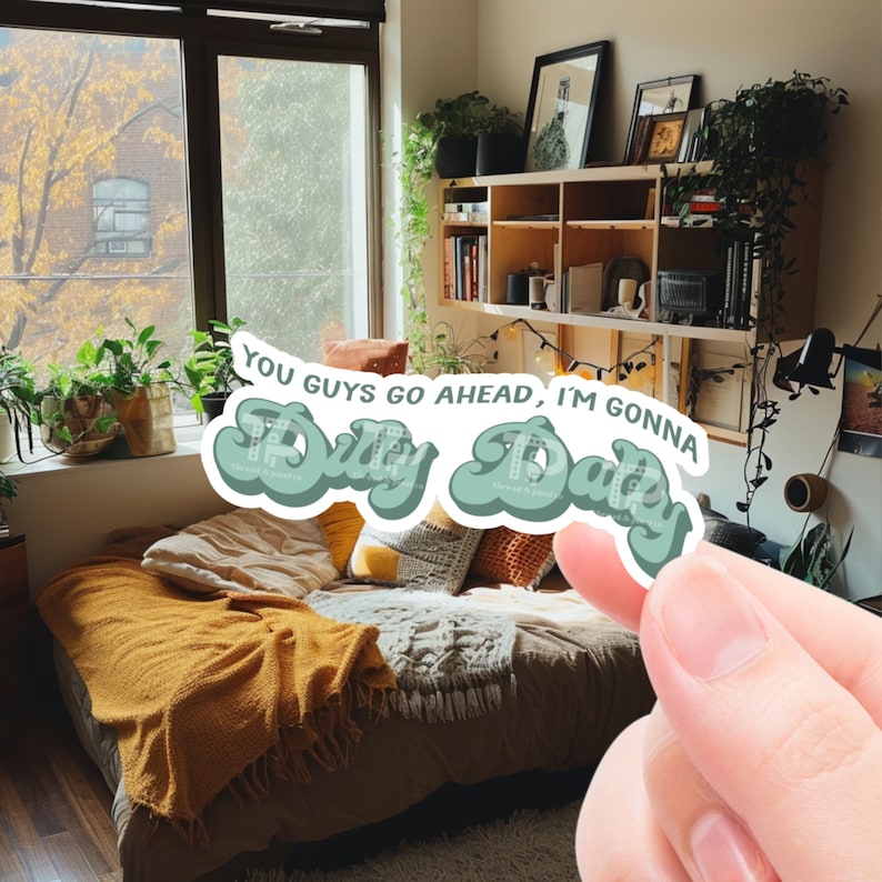 May include: A sticker with a retro design featuring the text "You guys go ahead, I'm gonna stay cozy." The sticker is in a light green color and has a white outline.