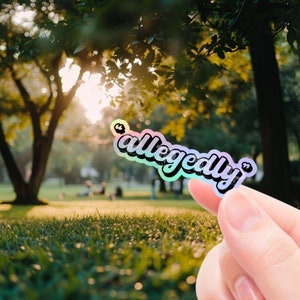 K&ouml;nnte beinhalten: Ein holografischer Aufkleber mit dem Wort "angeblich" in einer Regenbogen-Schriftart.