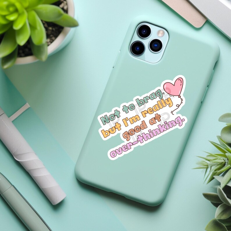 Op de afbeelding: Een lichtgroene telefoonhoes met een sticker waarop staat: "Niet om op te scheppen, maar ik ben echt goed in overdenken."