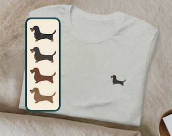 May include: A grey t-shirt with a black dachshund silhouette printed on the front. A separate image shows four dachshund silhouettes in different colors: black, brown, light brown, and dark brown.