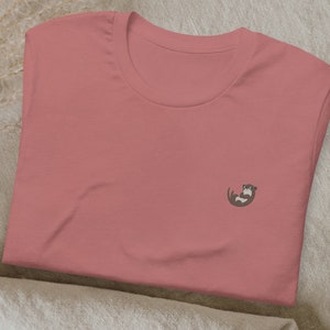 May include: A pink t-shirt with a small embroidered otter design on the front.