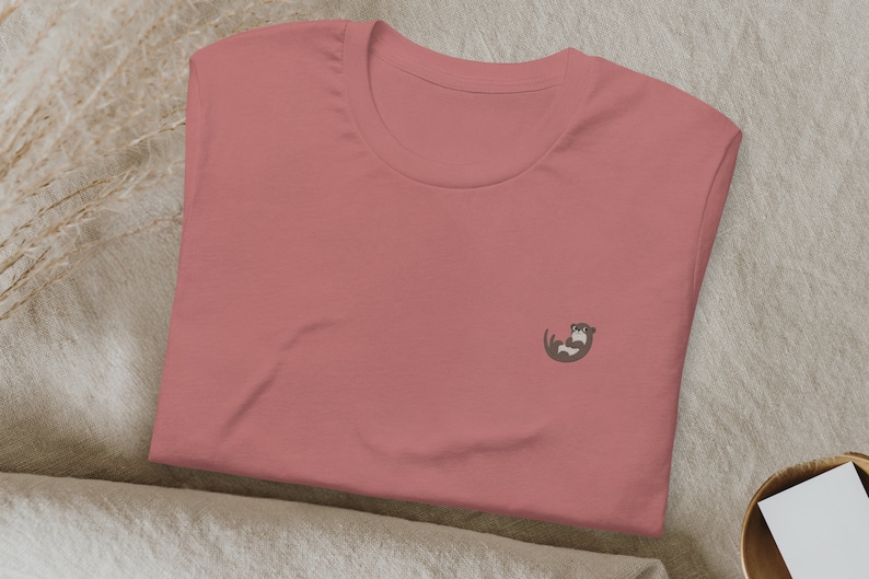 May include: A pink t-shirt with a small embroidered otter design on the front.